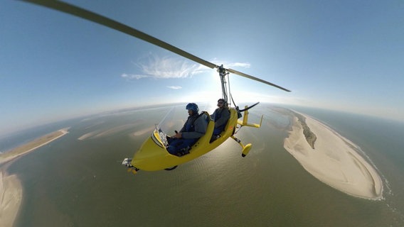 Zwei Personen fliegen mit einem offenen Flugzeug über die Nordseeküste. © NDR 