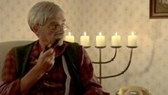 Ein älterer Herr mit grauem Schnauzer und Pfeife sitzt bei Kerzenschein in einem Sessel  