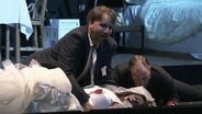 Opernszene: Zwei Männer beugen sich über eine am Boden liegende, verletzte Frau  