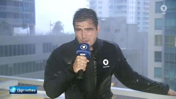 Reporter steht in einer Orkanböe und wird nass geregnet  