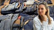 NDR Reporterin Ann-Brit Bakkenbüll schaut kritisch, im Hintergrund sieht man Jeans der Marke Levi's. © IMAGO /agefotostock / NDR 