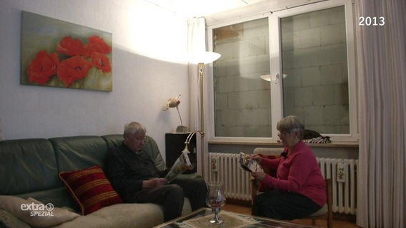 Ein älteres Paar sitzt vor einem zugemauerten Fenster.  