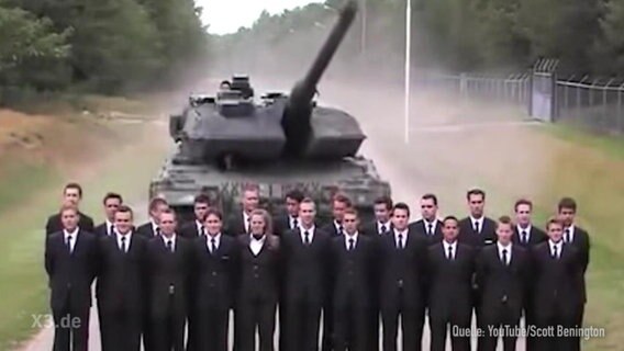 Ein Panzer, davor mehrere Männer in Anzügen.  