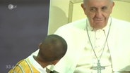 Ein Kind blickt den Papst an.  