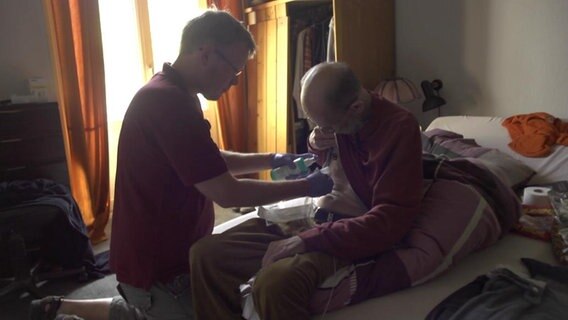 Ein Pfleger versorgt einen Patienten daheim.  