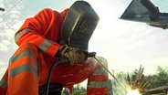 Ein Mann in Schutzkleidung arbeitet mit einem Schweißgerät an den Gleisen. © NDR/NDR/FrankTimmermann Foto: FrankTimmermann