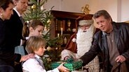 Weil der Weihnachtsmann Karim Himstedt (Horst Krause, 2.v.r.) zu betrunken ist, beschenkt Dirk Matthies (Jan Fedder, r.) Familie Lüthje: Mutter (Claudia Scheling), Vater (Steffen Ezold), Tochter Hendrike (Luisa Kroß) und Sohn Malte (Laurin Lüdke) bei der Bescherung. © NDR/ARD/Thorsten Jander 