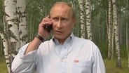 Russlands Präsident Putin steht in einem Wald und telefoniert mit einem  Handy.  