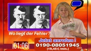 Ein Mann mit blonder Perücke steht neben zwei Fotos von Hitler..  
