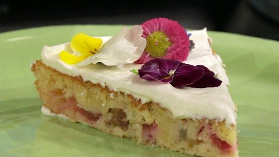 Ein Stück Rhabarberkuchen mit Sahne und Blüten dekoriert.  