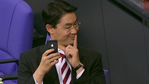 Politiker Philipp Rösler sitzt im Bundestag und schaut vermitzt auf sein Mobiltelefon.  