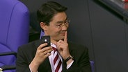 Politiker Philipp Rösler sitzt im Bundestag und schaut vermitzt auf sein Mobiltelefon.  