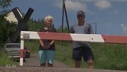 Herr und Frau Winkler stehen an der Bahnschranke Rothschönberg.  