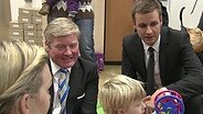 Tobias Schlegl kniet mit Bildungsminister Althusmann zwischen spielenden Kindern  
