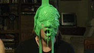 Der Kopf eines Menschen wird mit grünem Schleim übergossen.  