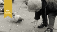 Kind füttert Tauben auf einem Platz (1962).  