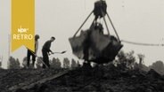 Baggerschaufel und zwei Bauarbeiter mit Schaufeln beim Deichbau 1962.  