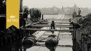Bauarbeiter bei Verlegung von zwei dicken Rohrleitungen  über die Alster 1962.  