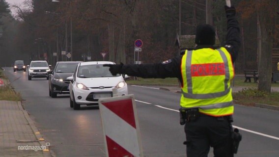 Ein Polizeibeamter winkt Verkehrsteilnehmer aus dem Verkehr raus.  