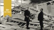 Zwei Männer stehen auf der herunter gekommenen Kassettendecke in einer Schulaula (1963)  