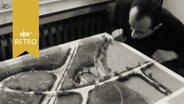 Besucher einer Ausstellung von Modellen für Landschaftsplanung betrachtet ein Modell von der Tischkante aus (1963)  