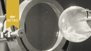 Versuchsanordnung in einem Labor: Eine Glaskugel vor einer Schelle bzw. einem Durchlass (1963)  