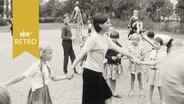 Erzieherin beim Ringelreigen mit Kindern auf einem Spielplatz 1965  