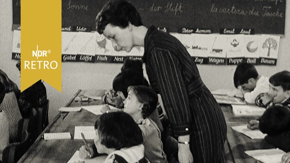 Lehrerin in einer Schule beugt sich über Schulkinder zur Kontrolle 1965  