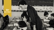 Lehrerin in einer Schule beugt sich über Schulkinder zur Kontrolle 1965  