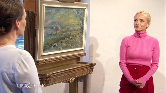 Zwei Frauen stehen neben einem Gemälde.  