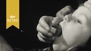 Kind bekommt einen Zuckerwürfel im Glas in den geöffneten Mund geschüttet (Schluckimpfung 1963)  