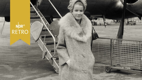 Mannequin führt einen Wintermantel der Kollektion 1963/64 auf dem Rollfeld des Hamburger Flughafens vor  