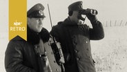 Zwei Beamte des Bundesgrenzschutz an der Zonengrenze, einer blickt durch ein Fernglas (1963)  