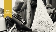 Taucher inspiziert ein Netz, das zu Wasser gelassen werden soll (1964)  