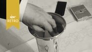 Hand greift in einen Pokal, um ein Los herauszuziehen (1965)  
