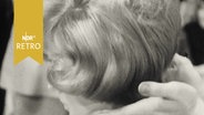 Frisur eines Modells bei der Friseurmeisterschaft 1965, Hände des Frisörs an ihrem Nacken  