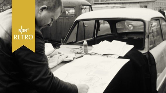 Wolf Vostell zeichnet auf der Motorhaube eines PKW auf einem Schrottplatz (Happening 1965 in Berlin)  