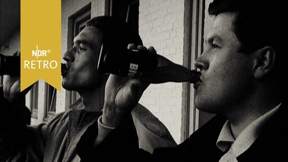 Junge Männer auf der Tribüne bei einem Fußballturnier trinken synchron Bier aus der Flasche (1965)  