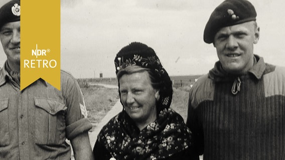 Zwei britische Soldaten posieren zum Foto mit einer Schleswig-Holsteinerin in traditioneller Tracht (1965)  