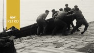 Soldaten ziehen beim Manöver ein Motorboot an Land (1965)  