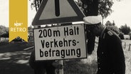 Polizisten stellen ein Warn-Schild an einer Landstraße zur "Verkehrszählung" auf (1965)  