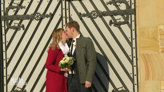 Ein frischvermähltes Ehepaar küsst sich vor einem Holztor.  