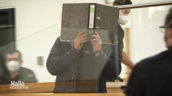 Der Angeklagte verbirgt sein Gesicht während der Verhandlung hinter einem Aktenordner.  