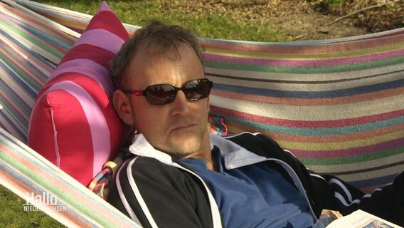 Ein Mann liegt auf einer Hängematte in der Sonne. Er trägt eine Sonnenbrille.  