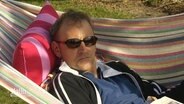 Ein Mann liegt auf einer Hängematte in der Sonne. Er trägt eine Sonnenbrille.  