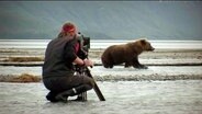 Ein Kameramann filmt aus nächster Distanz einen Bären.  