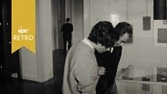 Besucher beugen sich über eine Vitrine in einer Ausstellung (Museum für Kunst und Gewerbe, Hamburg 1964)  