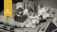 Modell mit Spielzeugautos und Häusern, das eine Wohnhausexplosion simuliert, die Rauchschwaden sind aus Watte (1964)  
