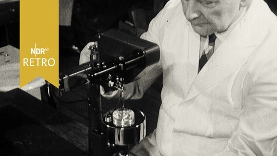 Mann mit weißem Kittel an einem Mikroskop (1964)  