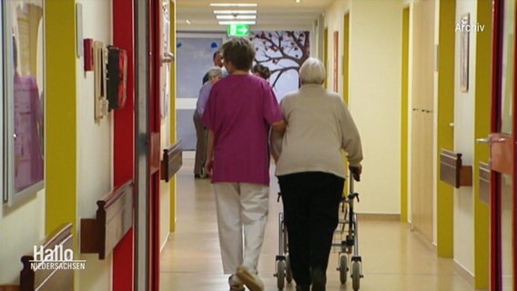 Eine Pflegerin begleitet eine Seniorin durch einen Pflegeheim-Flur  